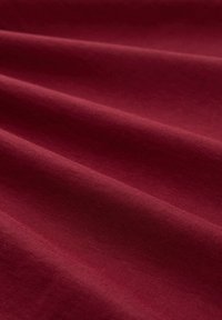 Bordeaux-stof met een gladde textuur, met subtiele kreuken en plooien die diepte en dimensie op het oppervlak creëren.