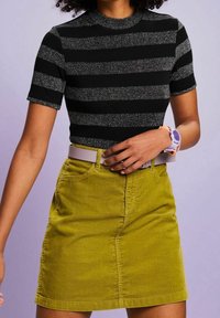 Lyhythihainen musta ja hopearaitainen toppi, joka on yhdistetty sinapinkeltaiseen corduroyo hameeseen. Varusteena valkoinen vyö ja violetti kello.