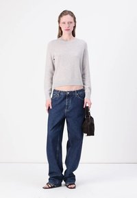 Maglione grigio chiaro a maniche corte, jeans scuri larghi, sandali neri e una piccola borsa marrone. Design semplice, minimal con dettagli ridotti, vestibilità rilassata.