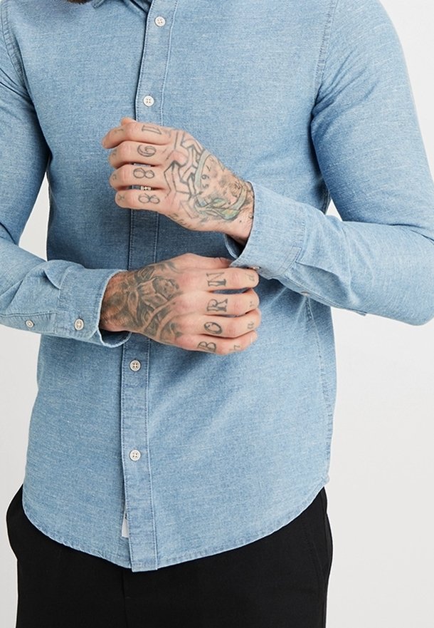 Camisa azul claro de manga larga hecha de tela de mezclilla. Presenta un dobladillo redondeado y detalles sutiles de costura.