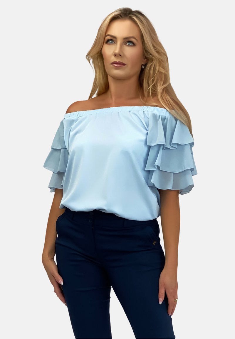 Jasnoniebieska bluzka odsłaniająca ramiona z warstwowymi rękawami w falbanki, gładki materiał, luźny krój, w zestawieniu z ciemnoniebieskimi spodniami.