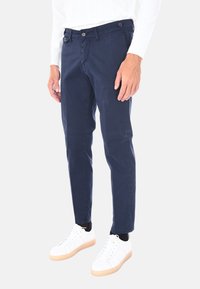 Chino blu navy con vestibilità slim, dotati di due tasche frontali, chiusura a bottone e una trama del tessuto sottile. Abbinati a sneakers bianche.