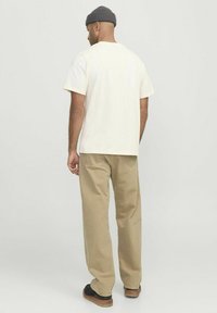 Creme bomulds t-shirt med korte ærmer, parret med beige bukser med brede ben. Modellen bærer en grå strikket beanie og sorte fodtøj.
