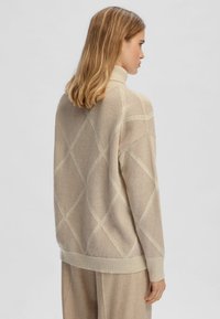Maglione lavorato a maglia beige con colletto alto, caratterizzato da un motivo a rombi in tonalità più chiare. Morbida texture e vestibilità comoda con polsini a costina.