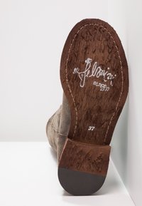 Chaussure en daim marron avec un talon en bois texturé, arborant un logo signature et la taille "37" imprimée sur la semelle.