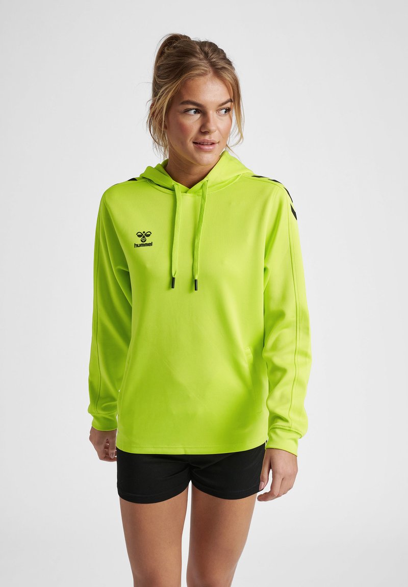 Heldere limoengroene hoodie met verstelbare koordjes, zwart logo en accenten, lange mouwen en een relaxed fit, gecombineerd met zwarte shorts.
