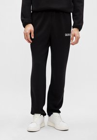 Czarne dresy o luźnym kroju, z elastycznym pasem i białym logo "CALVIN KLEIN" na lewym biodrze; w połączeniu z białymi trampkami.