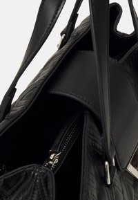 Black leather handbag with a quilted texture, featuring a zippered compartment and smooth accents, showcasing a structured design and dual handles.