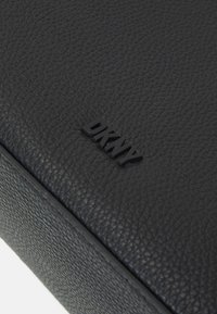 Svart strukturerat läderplånbok med en präglad DKNY-logotyp på framsidan. Ytan har en pebblig finish med rena kanter och sömmar.