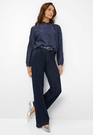 Camicia a maniche lunghe blu navy con motivo testurizzato e chiusura con bottoni, abbinata a jeans scuri a gamba larga e ballerine argentate a punta.