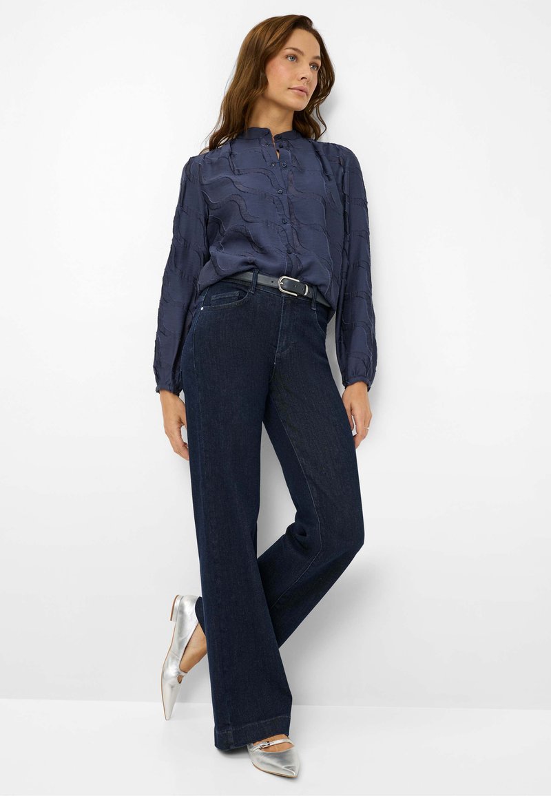 Camicia a maniche lunghe blu navy con motivo testurizzato e chiusura con bottoni, abbinata a jeans scuri a gamba larga e ballerine argentate a punta.