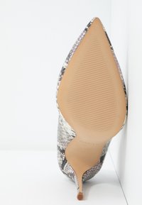 Chaussure à talon haut à bout pointu avec motif peau de serpent, semelle beige et talon aiguille fin sur un fond d'angle blanc.