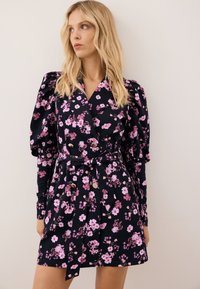 Bloemige jurk met een donkerblauwe achtergrond en roze bloemen, lange pofmouwen, een dubbelzijdige voorkant en een geknotte taille.