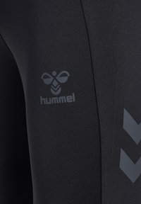 Gros plan d'un legging de sport noir avec logo abeille hummel réfléchissant et motifs chevrons sur la cuisse.