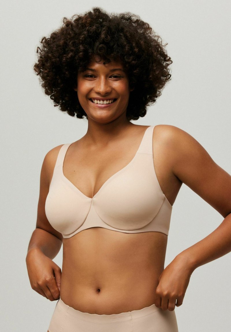 Sostén de color beige con aros, copas moldeadas, tirantes anchos y textura de tela suave. Modelo mostrando el ajuste con culotte a juego.