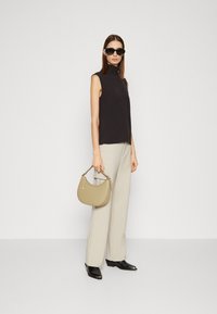Top nero senza maniche, pantaloni beige a gamba larga, stivaletti neri alla caviglia e una piccola borsa a tracolla marrone chiaro. Il modello indossa occhiali da sole neri.
