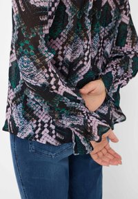 Langærmet bluse med slangeprint i sort, pink og grøn. Har flagrende manchetter og et let, flydende stof.