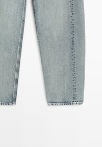 Lichtblauwe spijkerbroekspijpen met rechte snede en zichtbare naden, afgebeeld tegen een witte achtergrond.