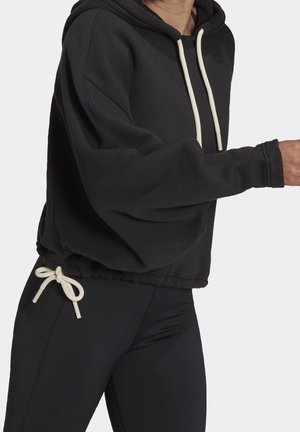 Osoba w czarnej bluzie z kapturem z białymi sznureczkami i czarnych legginsach, częściowo widoczna od szyi do połowy uda.