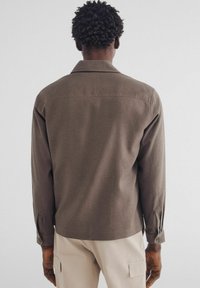 Bruine lange mouw blouse met een kraag en knoopmanchetten, met een zachte textuur en een relaxte pasvorm, gezien vanuit de achterkant.