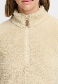 Beige fleece pullover with a high collar, quarter zip closure, and soft texture. Features a small brand tag near the zipper.