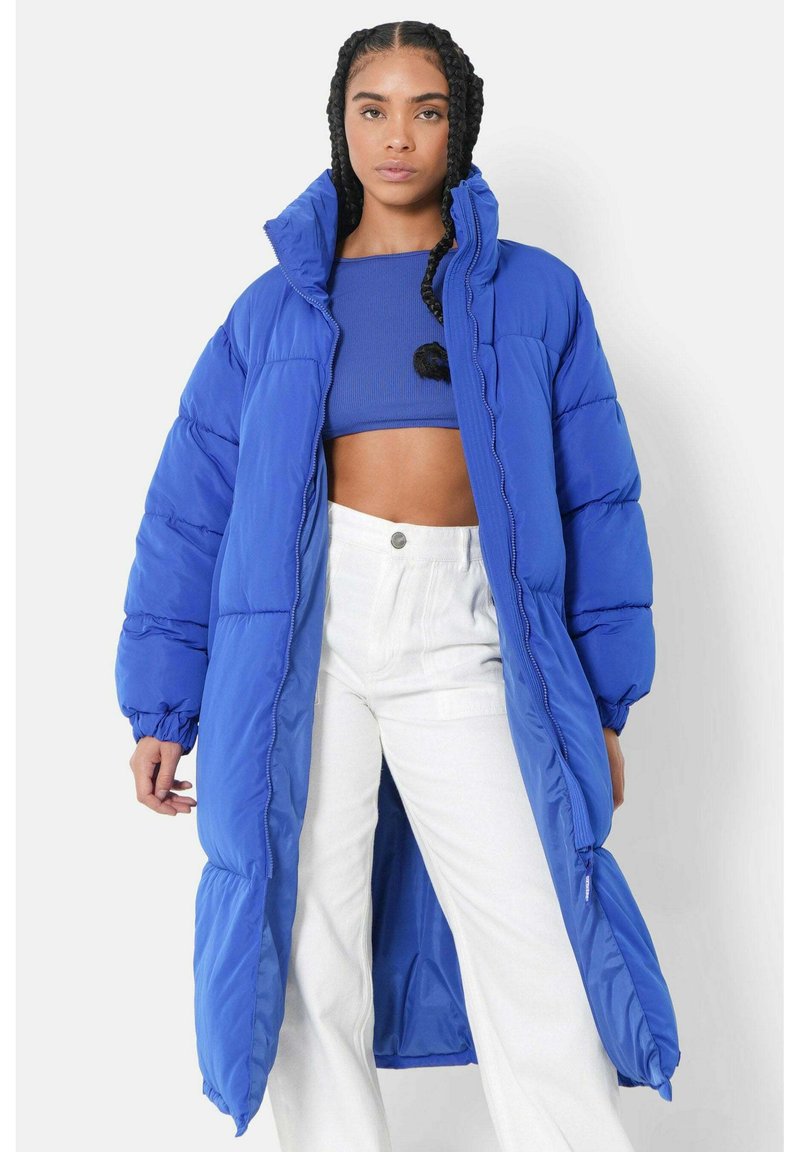 Longue doudoune bleue avec un col haut, des poignets élastiques et des poches latérales zippées, présentant une texture brillante et matelassée.