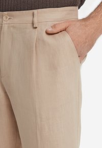 Beige linnedragtbukser med glat front, enkelt pres, sidelommer og bæltestrop med én knaplukning i taljen.