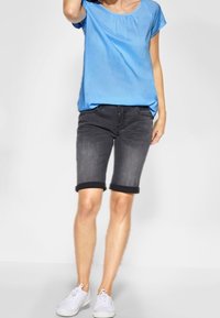 Lichtblauw topje met korte mouwen en een ronde hals, gecombineerd met donkergrijze denim shorts met opgerolde zoom. Witte sneakers maken de outfit compleet.