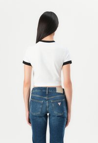 Hvit avkortet t-skjorte med svart halskant og ermekanter, parret med tettsittende mørkeblå denim jeans med baklommer og logo-patch.