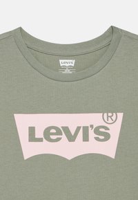 Ελαιόχρωμο μπλουζάκι με στρογγυλή λαιμόκοψη, που διαθέτει μεγάλο ροζ λογότυπο Levi's κεντραρισμένο στο στήθος. Μαλακή υφή και λεία φινίρισμα υφάσματος.