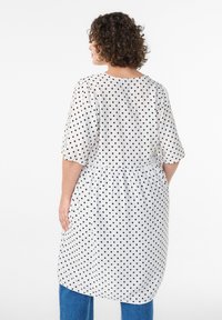 Valge kleit mustade täppidega, millel on ümmargune kaelus, lühikesed puhvärvid ja elastne vöökoht, ulatudes põlvedest allapoole.