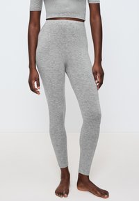 Šedé legíny vyrobené z měkké a elastické tkaniny, s vysokým pasem a hladkým povrchem, doplněné těsným střihem.