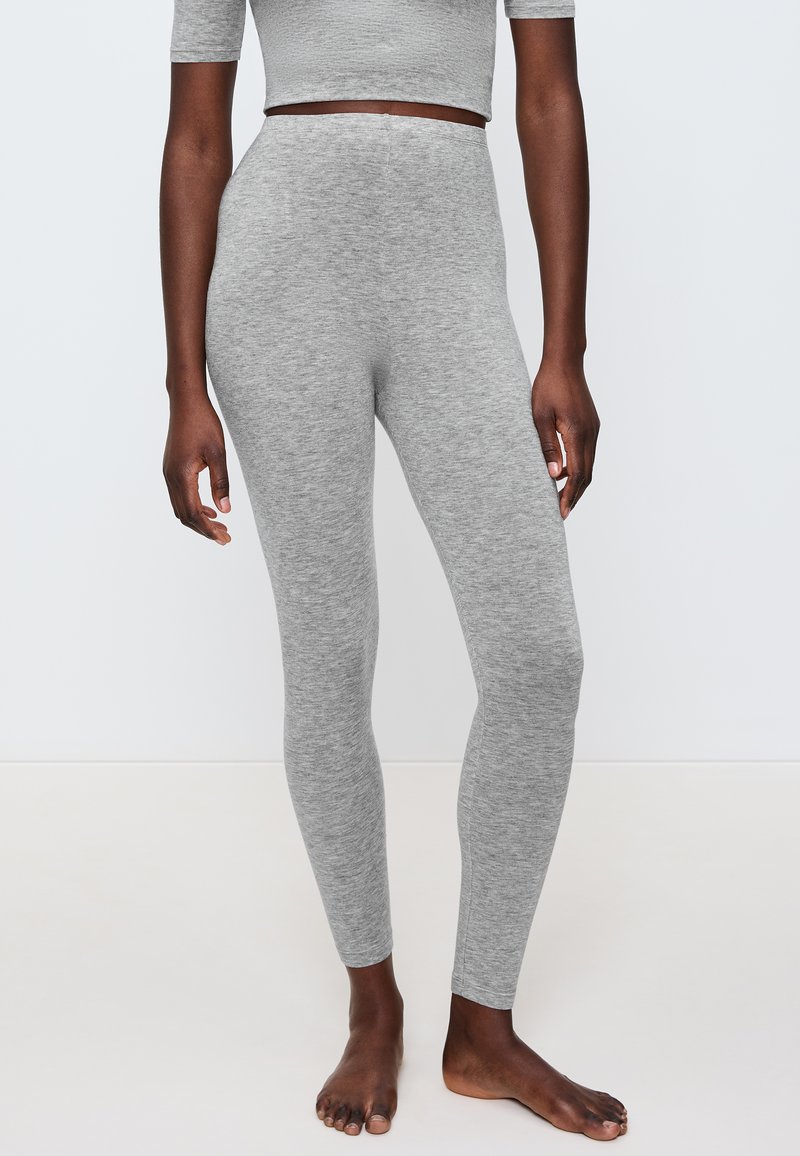 Šedé legíny vyrobené z měkké a elastické tkaniny, s vysokým pasem a hladkým povrchem, doplněné těsným střihem.