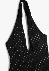Zwarte haltertop met een diepe V-hals, versierd met verspreide zilveren studs op de stof. Zacht materiaal met een gladde textuur.
