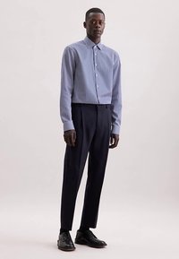 Gestreept overhemd met knopen in blauw en wit, gecombineerd met donkerblauwe broek. Zwart glanzend schoeisel. Eenvoudig ontwerp en op maat gemaakte pasvorm.