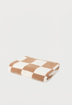 Serviette pliée avec un motif à carreaux beige et blanc, posée sur une surface blanche unie.