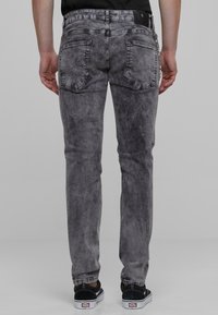 Šedé džínsy s vyblednutou textúrou, päť vreciek a slim fit strihom, doplnené čiernymi teniskami s bielymi podrážkami.