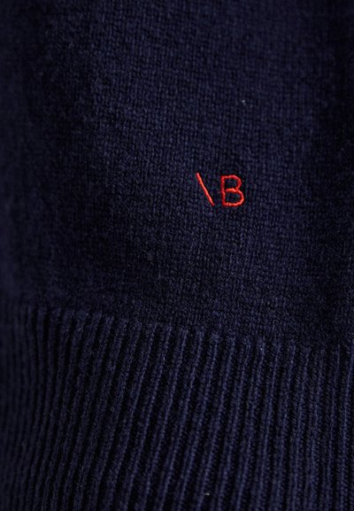 Jūrinės tamsiai mėlynos spalvos megztinis su rausvu tekstūruotu raštu, ant priekinės pusės išryškinta raudona išsiuvinėta „B“ detalė. Minkštas mezgimo audinys.