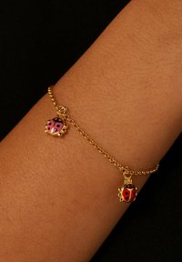Gouden armband met twee lieveheersbeestjes charm, een rode met zwarte stippen en een roze met zwarte details, rustend op een pols.