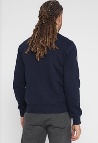 Sudadera azul marino con puños y dobladillo acanalados, que presenta un cuello redondo y detalles de hardware mínimos. Tejido suave y texturizado.