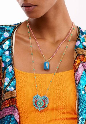 Deux colliers : l'un avec un pendentif rayé bleu et des accents dorés, l'autre avec un charme en forme de cœur multicolore sur une chaîne en argent.