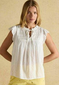 Weiße, leichte Bluse mit rüschierten Kurzärmeln, einem gerafften Ausschnitt und einem Bindeband. Glatte Textur mit lockerer Passform.