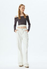 Grijs geribbeld off-shoulder crop top met crèmekleurige afwerking, gecombineerd met witte brede cargobroek met zijzakken en een knoopsluiting.