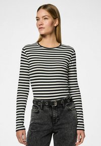 Top de rayas blanco y negro de manga larga con cuello redondo, textura acanalada, combinado con jeans de mezclilla negra de tiro alto y un cinturón negro.