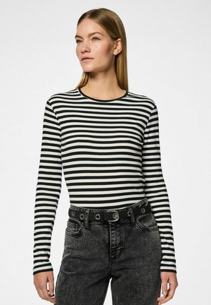Top de rayas blanco y negro de manga larga con cuello redondo, textura acanalada, combinado con jeans de mezclilla negra de tiro alto y un cinturón negro.