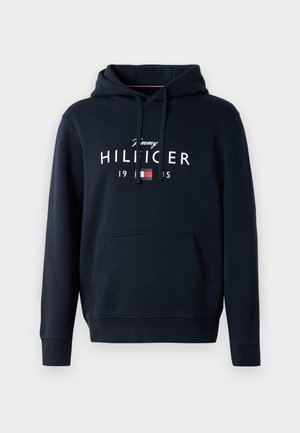 Marineblauwe hoodie van zachte stof, met een kangoeroezak, een capuchon met trekkoord en een wit tekstlogo met rode en blauwe accenten.