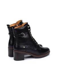 Botas de cuero negras hasta el tobillo con punta redondeada, parte delantera con cordones y un detalle de hebilla plateada. Taco grueso marrón con suela con relieve.
