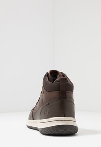 Zapatillas marrones de altura media con parte superior de cuero texturizado y malla, suela en contraste, tirador en la parte posterior y un sutil detalle de logo.