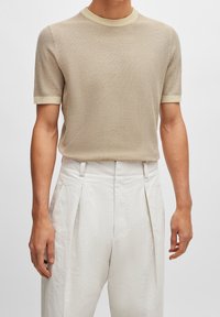 Chemise courte beige en tricot avec un col rond côtelé et une bordure contrastante jaune clair sur le col et les manches.