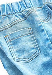 Lichtblauwe denim broek met een elastische tailleband, voorzien van een achterzak met contrast oranje stiksel en een gladde textuur.